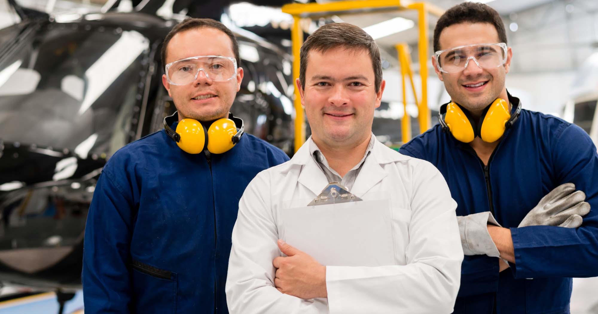 Three men in a factory with ear muffs on